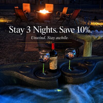 A hot tub with water flowing, a bottle of wine and two glasses. Behind it is a fire pit. The words say Stay 3 nights. Save 20%. Unwind, Stay awhile.