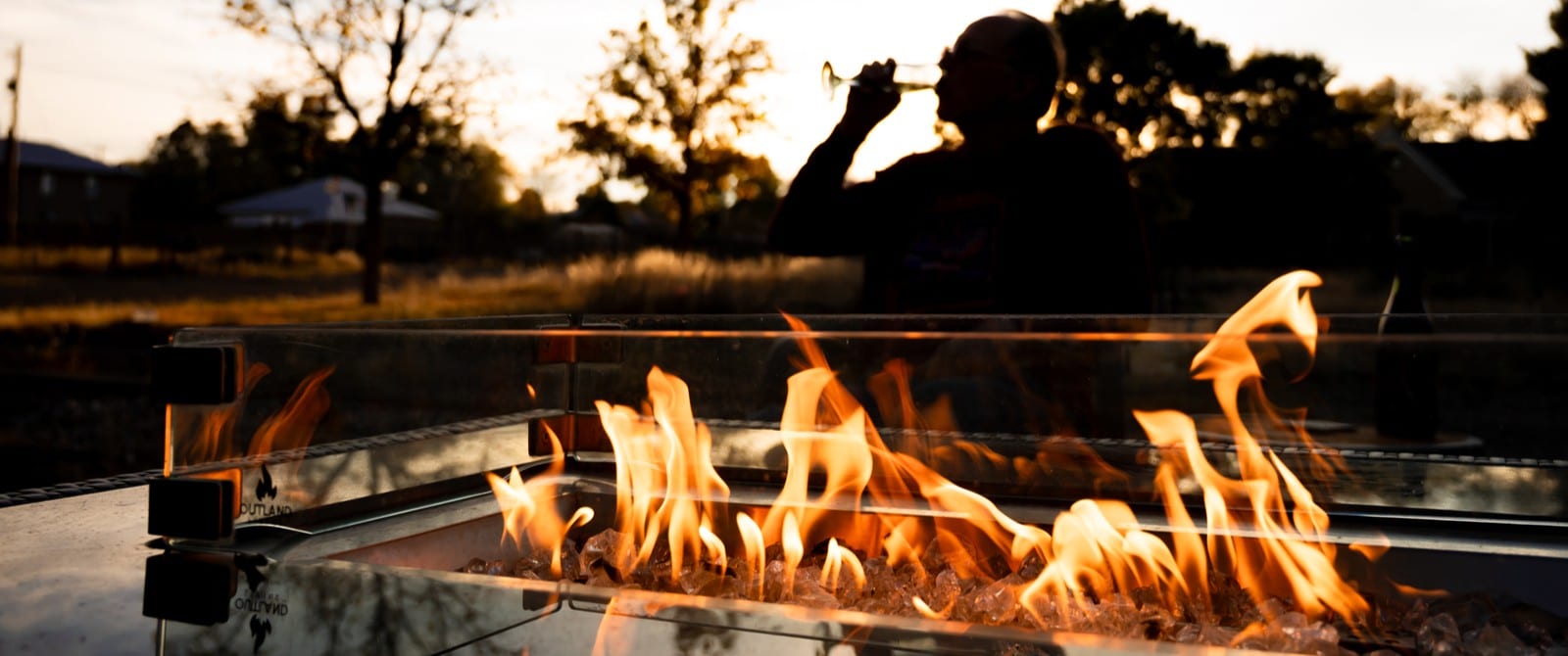 A fire in a fire pit at sunset, with a person drinking from a champagne flute in the background.