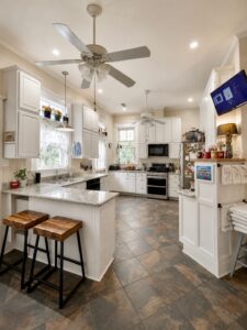 Present-day kitchen of the Kincaid-Wade House, expanded by former owners Jim and Cherry Jones, with white cabinetry, large windows and a breakfast bar with stools.