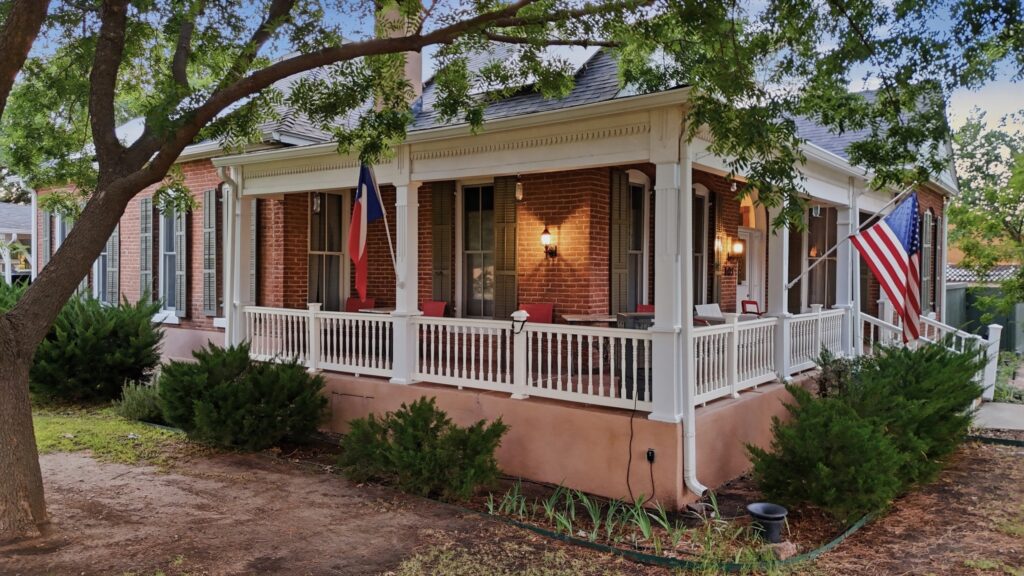 Present-day exterior of the Kincaid-Wade House in Alpine, Texas, showing its red-brick exterior and wraparound porch shaded by mature trees.