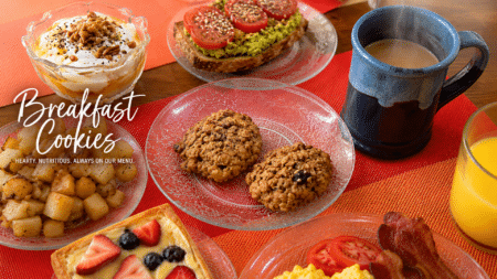 Breakfast spread on a red tablecloth with yogurt parfait, toast, cookies, fruit tart, and a steaming coffee mug.