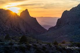 A sunset to the left of a view between two mountains. This is the view of the Window in Big Bend National Park