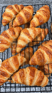 Fresh baked, flaky croissants cooling on a rack.