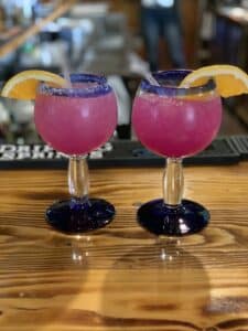 Beatiful pink-colored drinks in margarita glasses lined with salt and garnished with an orange slice.