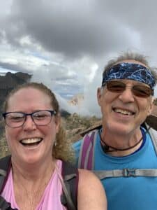 A man and a woman laughing, in front of low clouds that look like a heart.