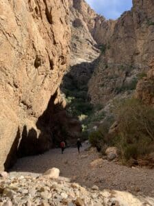 People walking in a dry creek bed surrounded by high cliffs