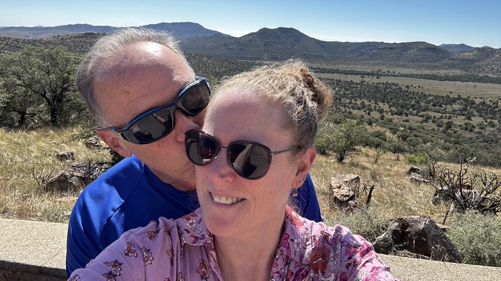 A selfie of two people in front a valley and mountains