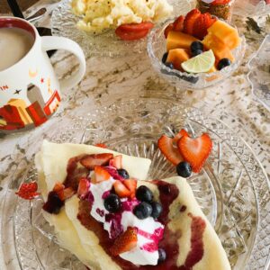 Ricotta filled crepes with whipped cream and berries, coffee, fresh fruit, scrambled eggs