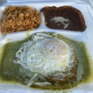 Flat enchiladas with green sauce and a fried egg on top, and sides of beans and rice