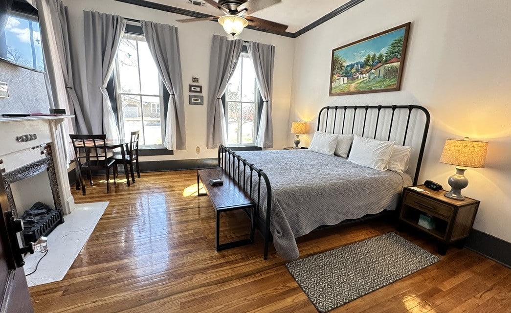 Beautiful bedroom with large windows, table with two chairs and TV on the wall above an electric fireplace