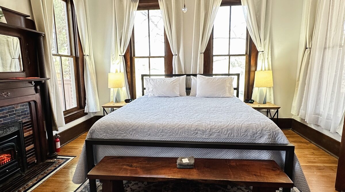 bedroom with king bed, windows on three sides, morning light, fireplace, bench