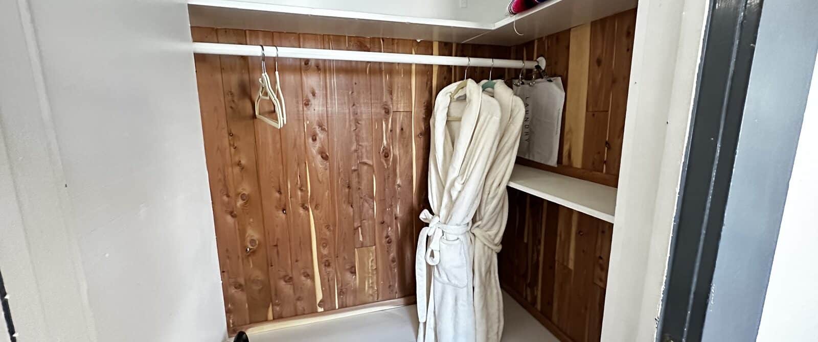 Cedar-lined closet with two robes, shelves, blanket and luggage rack