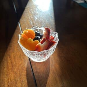 A small bowl of fruit on a wood table covered by a beam of strong sunlight.