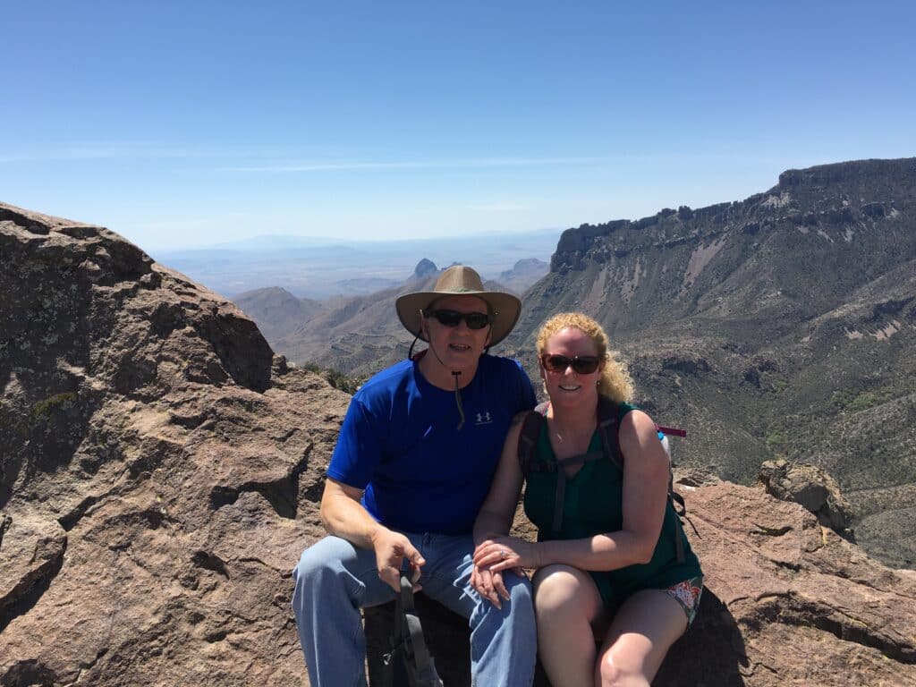 Two people sitting on a rock with mountains and blue skies in the background