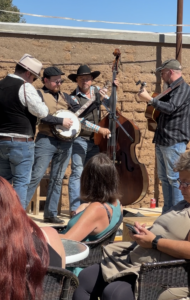 People sitting outdoors on a sunny day, watching a band play