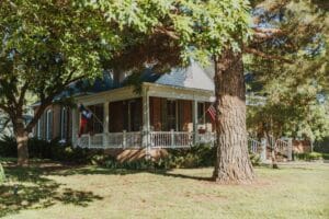 red-brick home with wrap-around porch nestled between trees