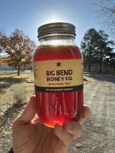 A bottle of dark amber honey held up in front of the sun, with a label that says Big Bend Honey Co.