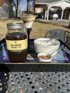 a parfait glass with what looks like yogurt, honey and nuts. a bottle with what looks like honey with a label that says Big Bend Honey Co. A large glass bowl with yogurt in it.
