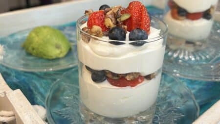 A glass filled with what looks like yogurt, layered like a parfait with fruit and granola.