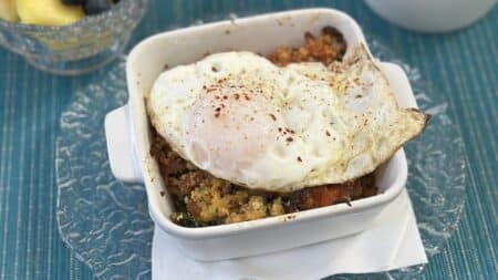 a sqaure white ceramic dish filled with what looks like crumbled bread, topped with a fried egg.