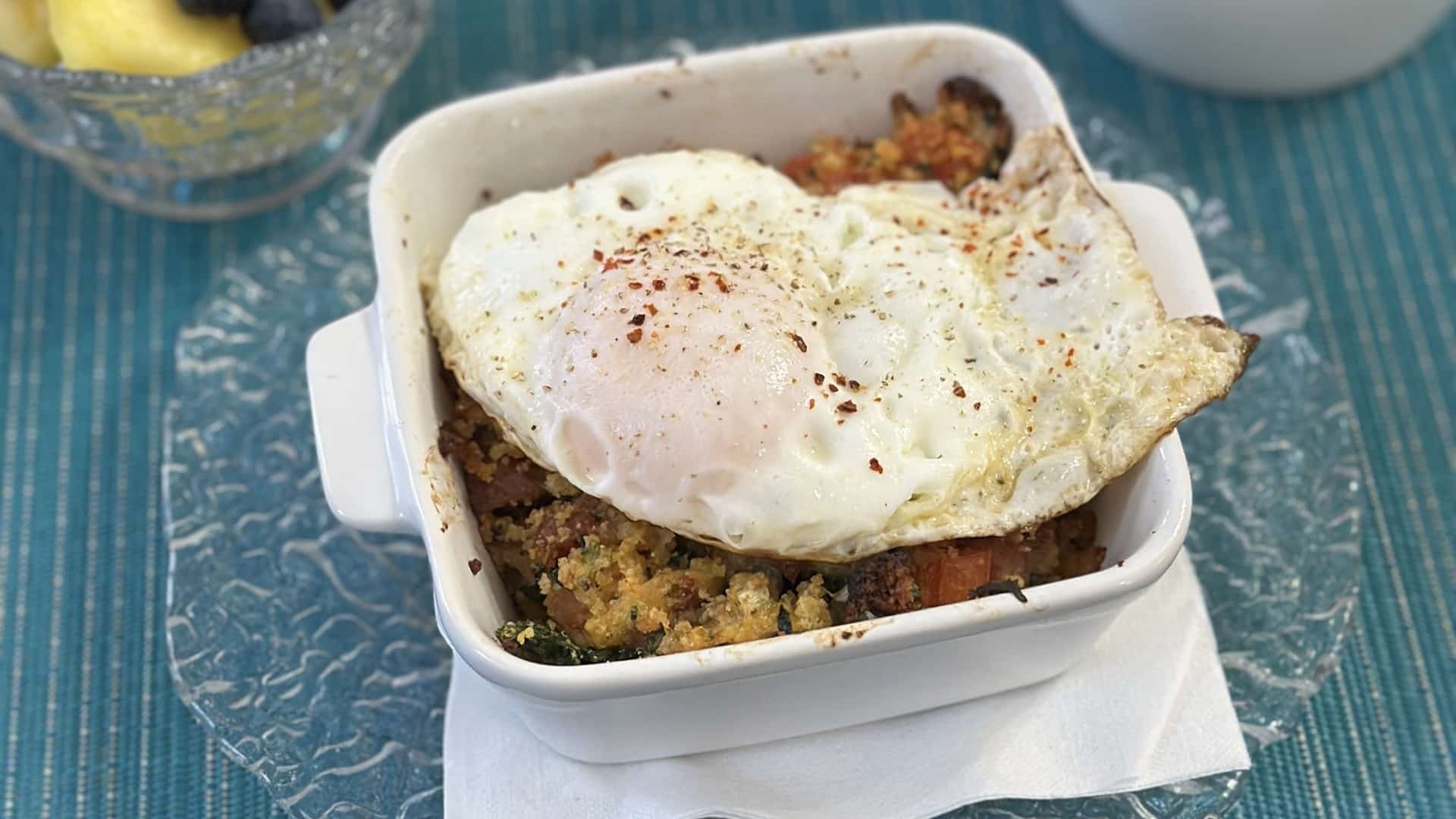 a sqaure white ceramic dish filled with what looks like crumbled bread, topped with a fried egg.