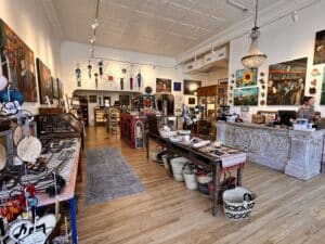 A large room filled with art on the wall and tables, with nice lighting and hardwood floors