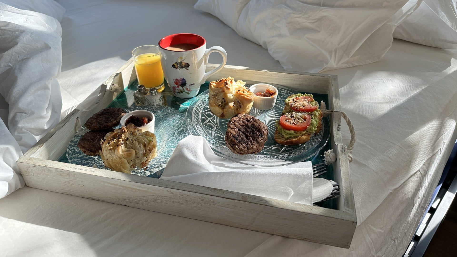 Breakfast on a tray including sausage, coffee, orange juice, a puff pastry, avocado toast