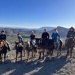 6 people on horseback in front of mountains with clear blue skies