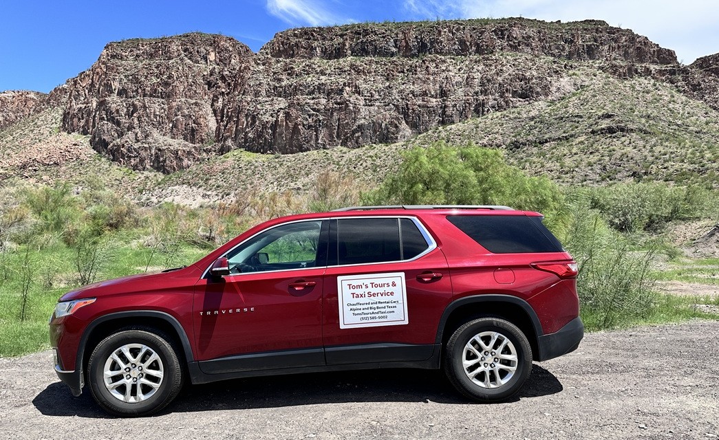 a red Chevy Traverse with a sign that says Toms Tours and Taxi. There is a mountain behind it.