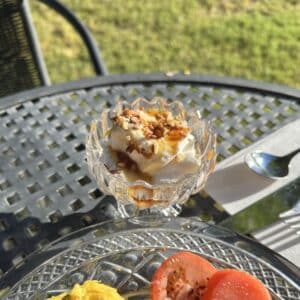 a tulip shaped bowl with what looks like yogurt topped with honey and nuts sitting on a table outside in the sun.