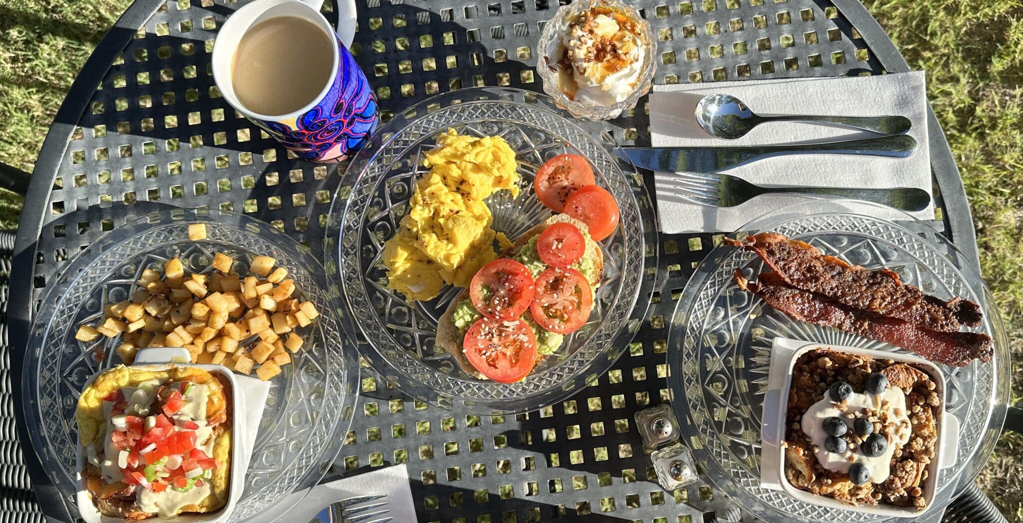 a table laid out with breakfast foods like eggs, avocado toast, bacon, coffee, yogurt, potatoes
