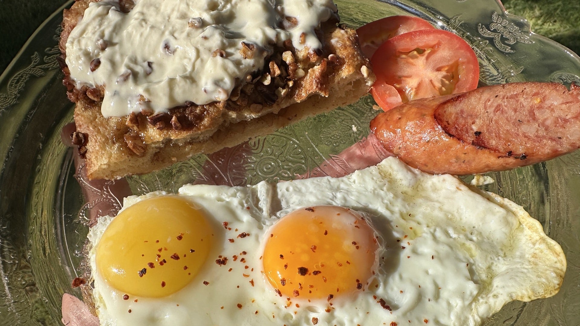 Two fried eggs, tomatoes, sausage, and a pastry with white icing