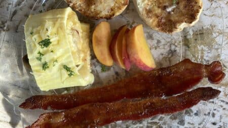 A plate of eggs, peach slices, English muffins, and bacon