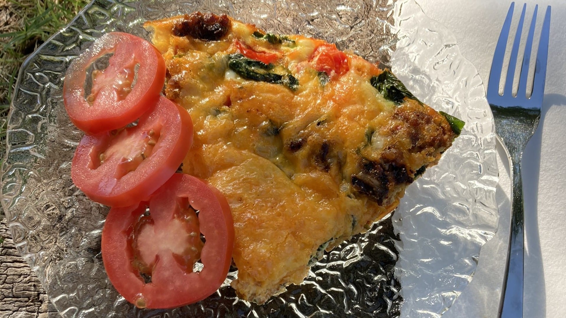a plate with a slice of what looks like quiche with a side of sliced tomatoes