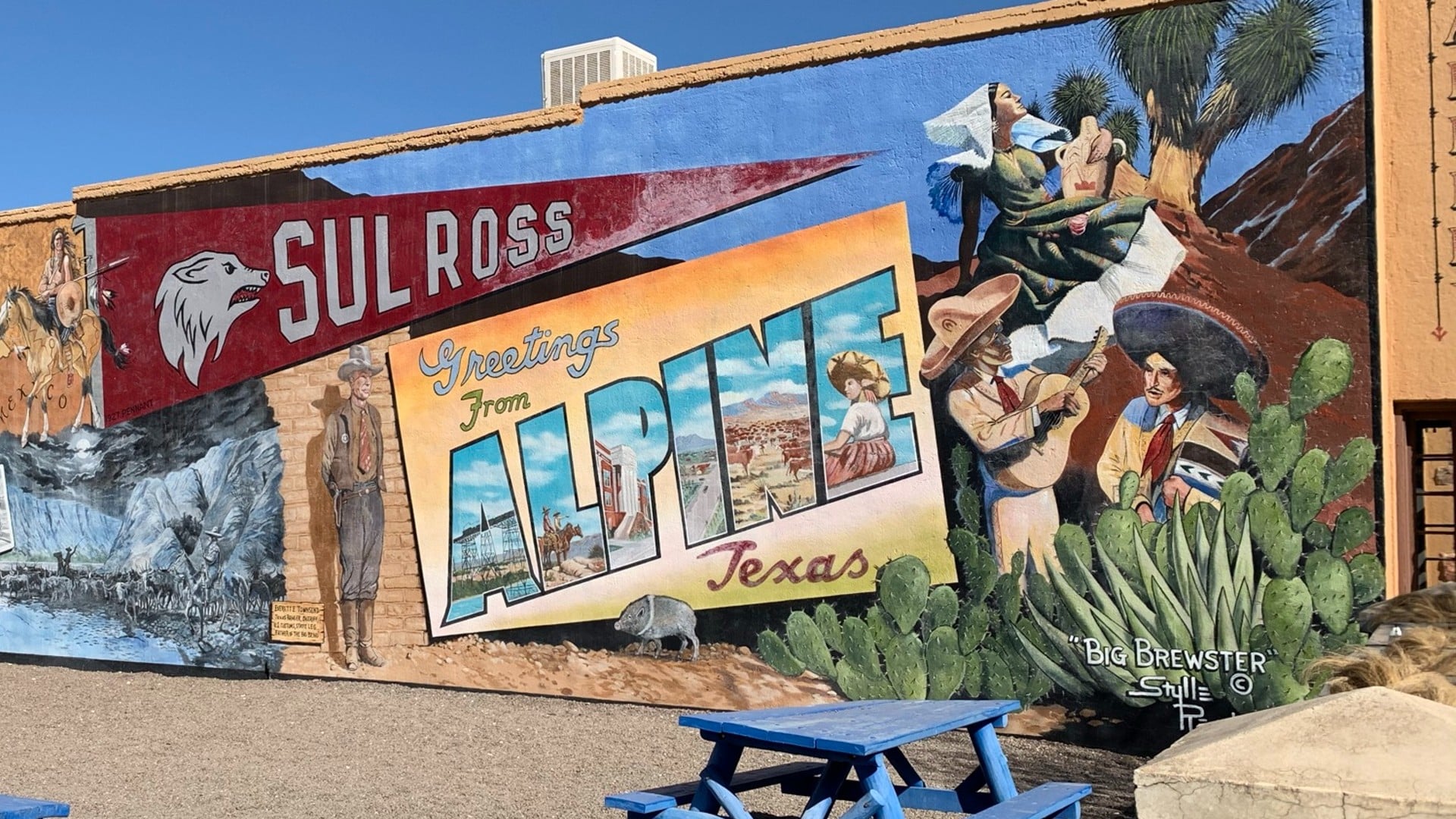 A large colorful mural on the side of the building depicting a postcard to visit a local town