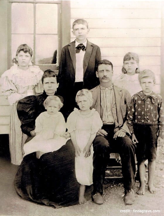 Black and white historic photograph of a family of eight outside of a home