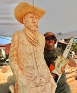 Chainsaw carving of a cowboy with the artist standing next to him