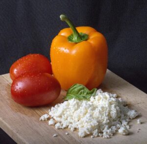 a yellow pepper, two red roma tomatoes and a pile of grated white cheese with some green leaves on top