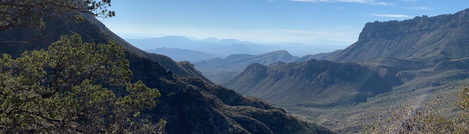 An expansive mountain range and valley covered in trees with blue skies above