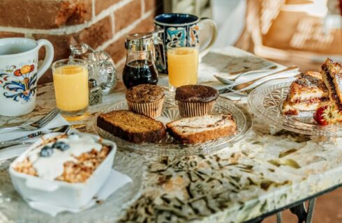 Square table with plates of breakfast items, cups of orange juice and two mugs of coffee