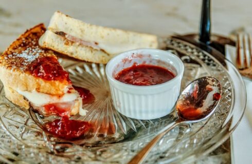 Glass plate with a Monte Cristo sandwich and a spoon by a white cup of jam