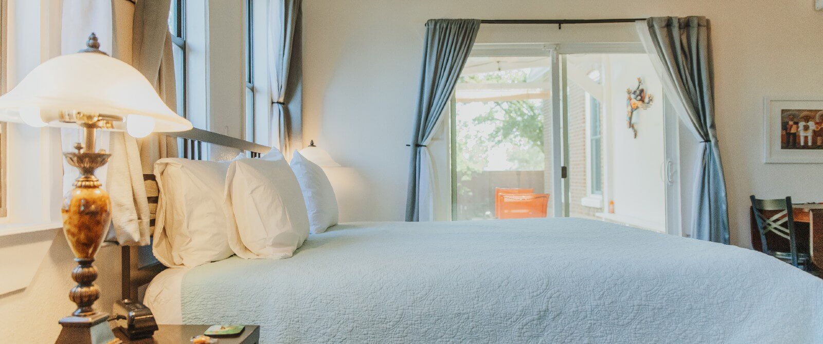 A bright bedroom with a king bed, side tables with lamps and sliding door to an outdoor patio