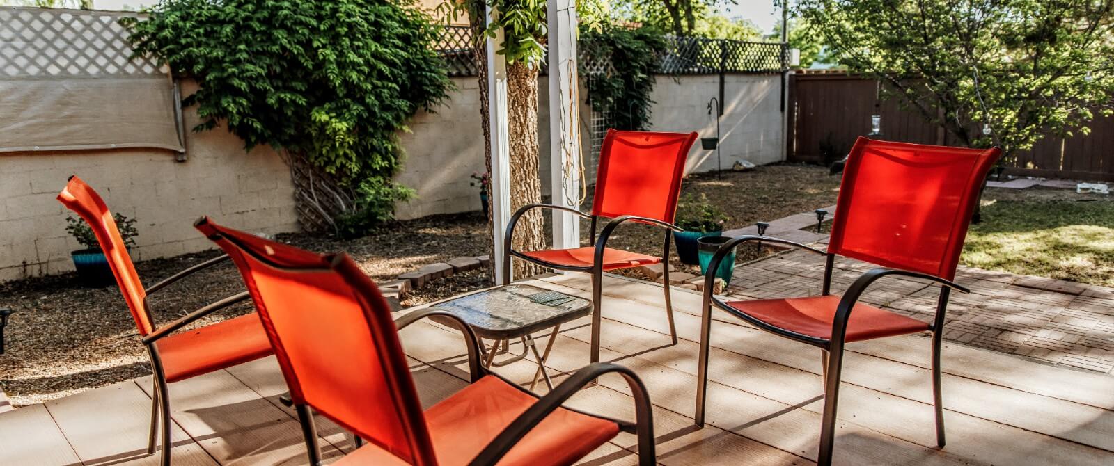 An outdoor fenced patio with four red chairs and a small table
