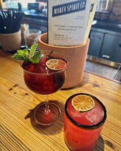 Two drinks that are reddish in color with dried citrus slices in them, in front of a menu that Marfa Spirit Co.