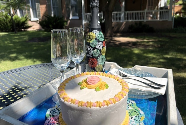 Outdoor table with a white birthday cake with two flute glasses and a bottle of champagne