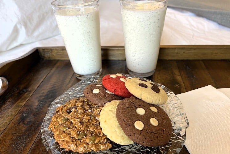 A wood platter with two glasses of milk and a glass plate of cookies